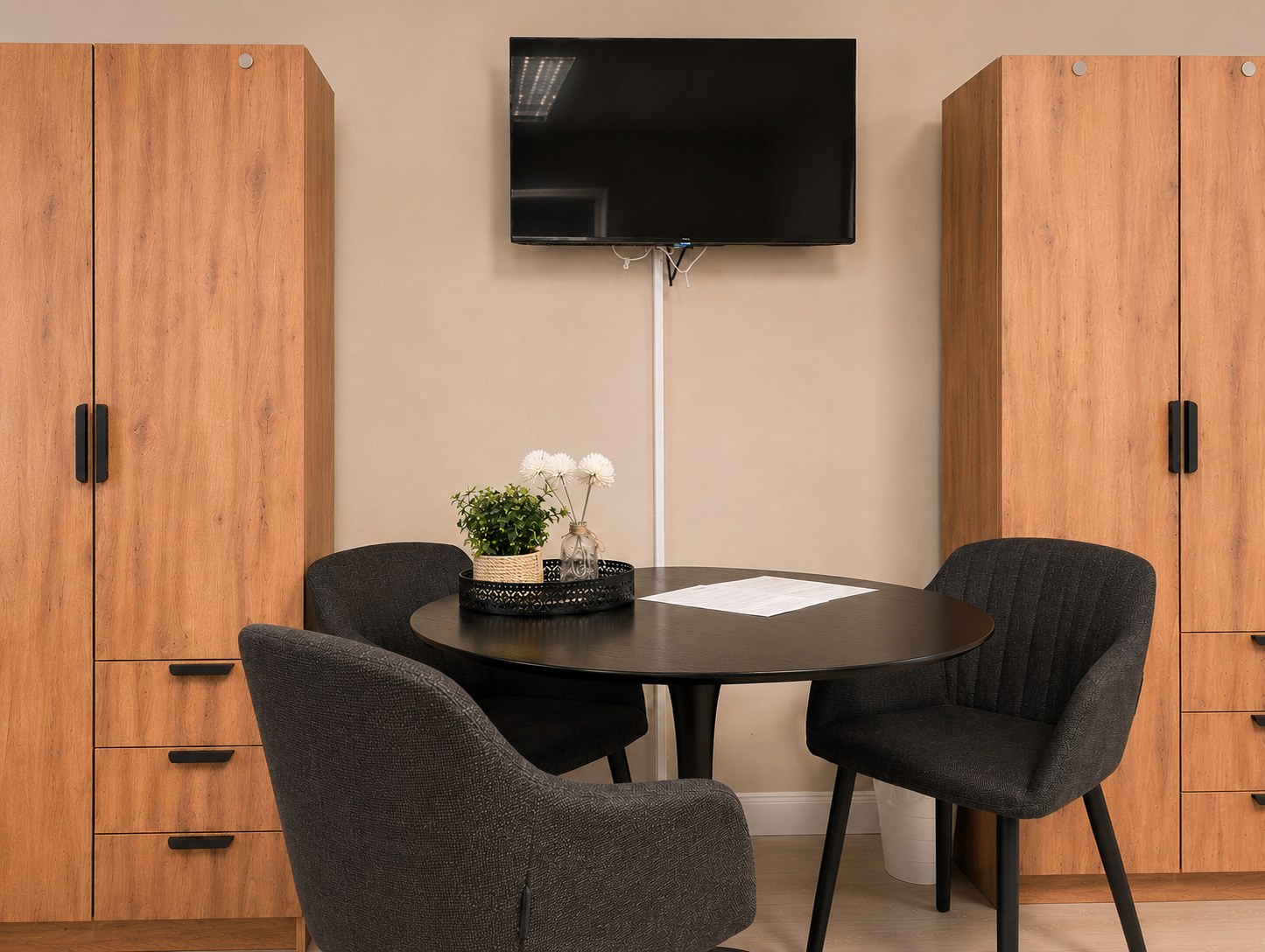 Gemütlicher Sitzbereich mit Tisch, Fernseher und Schränken im modernen Dreibettzimmer der HK Vermietung in Brieselang.